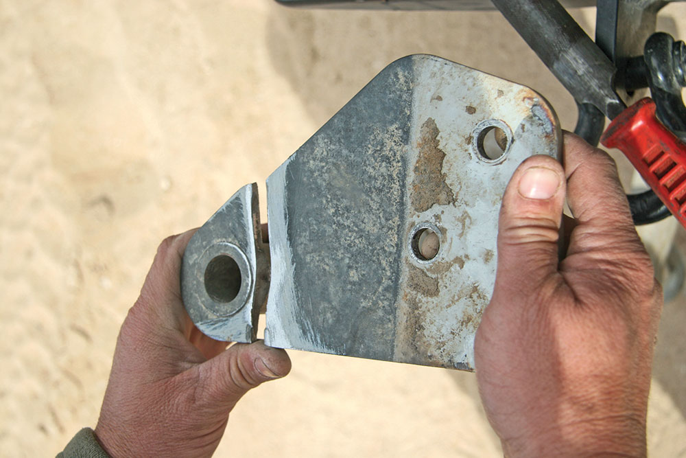 A man's calloused hands hold a broken metal suspension bracket.