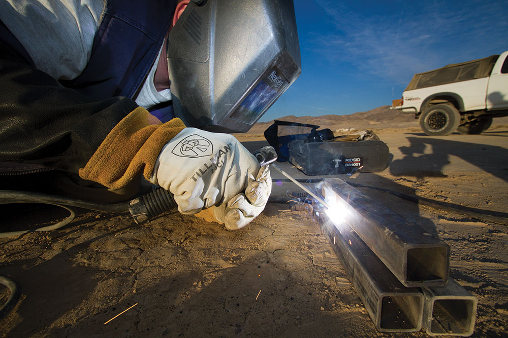 A person wearing a welding hood fuses together three metal bars.