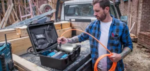 A man in a blue shirt uses the compressor with an orange tube.