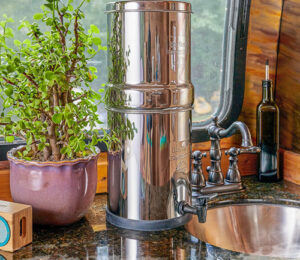 The water filter sits on a camp trailer's kitchen counter next to a plant.