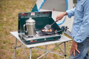 A camp kitchen setup features the small grill and water kettle.