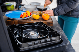 A camper cuts vegetables on a tailgate camp kitchen setup.