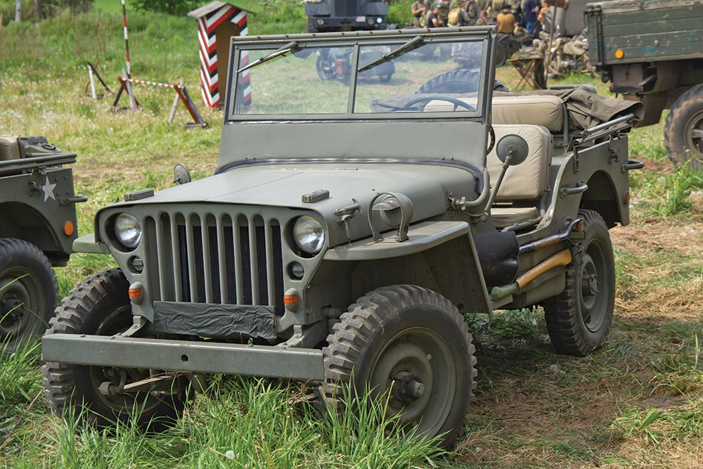 A color photo of an early Jeep; doorless and roofless, it is painted matte green and has a tan leather bench seat.