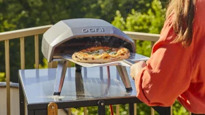 A woman removes pizza from the metal oven.