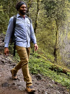 A guy in a long sleeve blue button down shirt and tan pants hikes downhill.