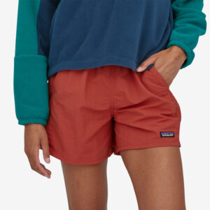 A gal in a blue sweatshirt puts her hand in the pocket of red shorts.