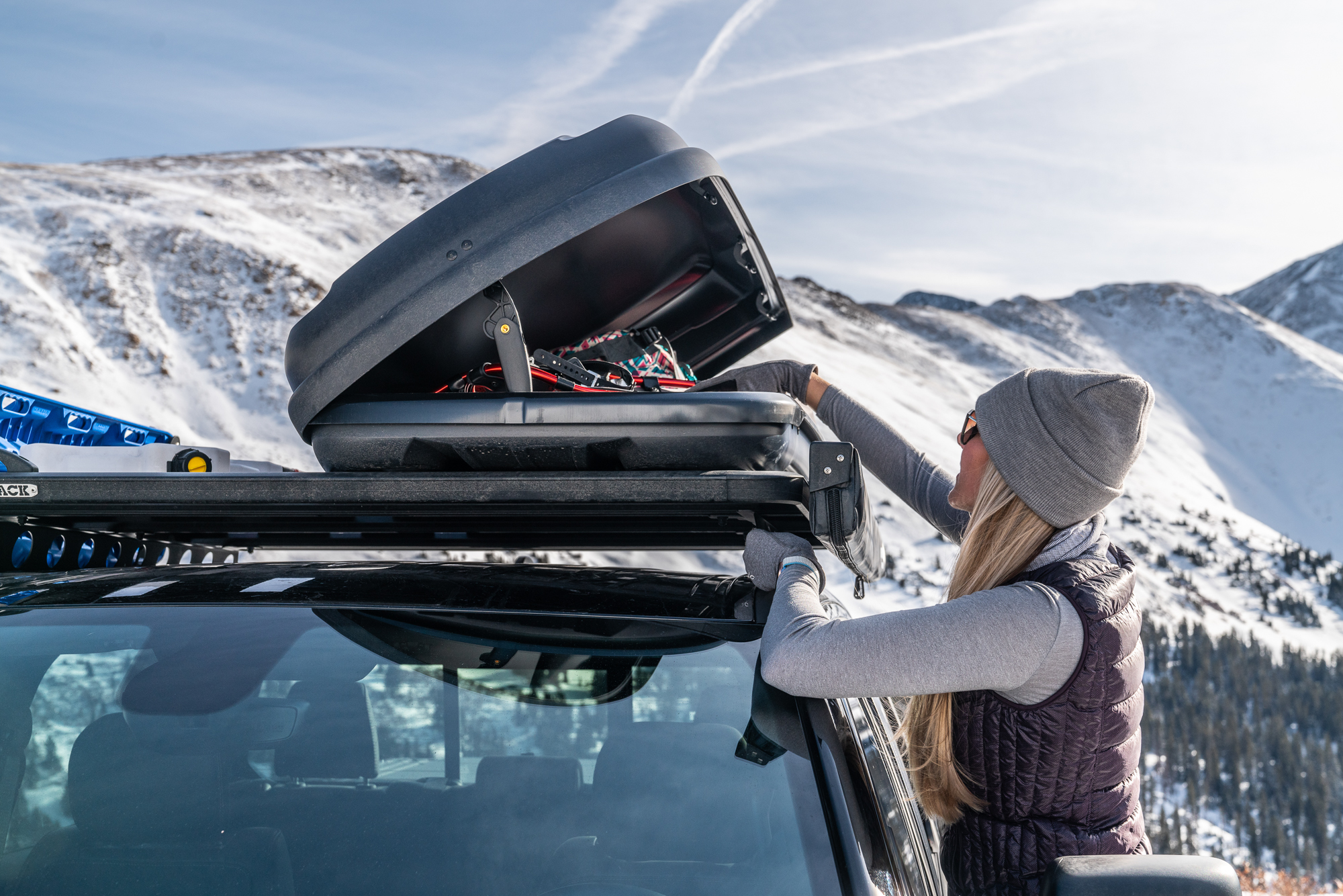 Woman loading gear into car roof cargo box.