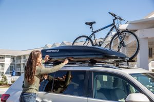 Woman closing roof top storage case on top of white car.