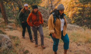 Three gals hike upward along a trail path in the fall.