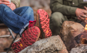 Someone in jeans and boots with red soles rests their feet on a rock.