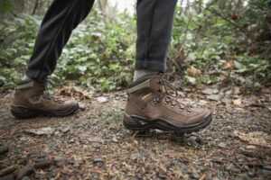 Someone walks on a dirt path in brown hiking boots.