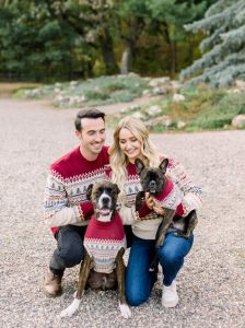 Famil of a woman, man and two dogs pose smiling with matching sweaters