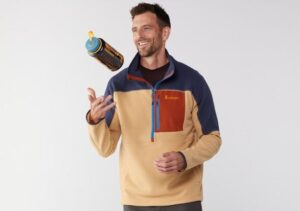A guy in a blue and tan sweatshirt tosses a water bottle in the air while modeling.