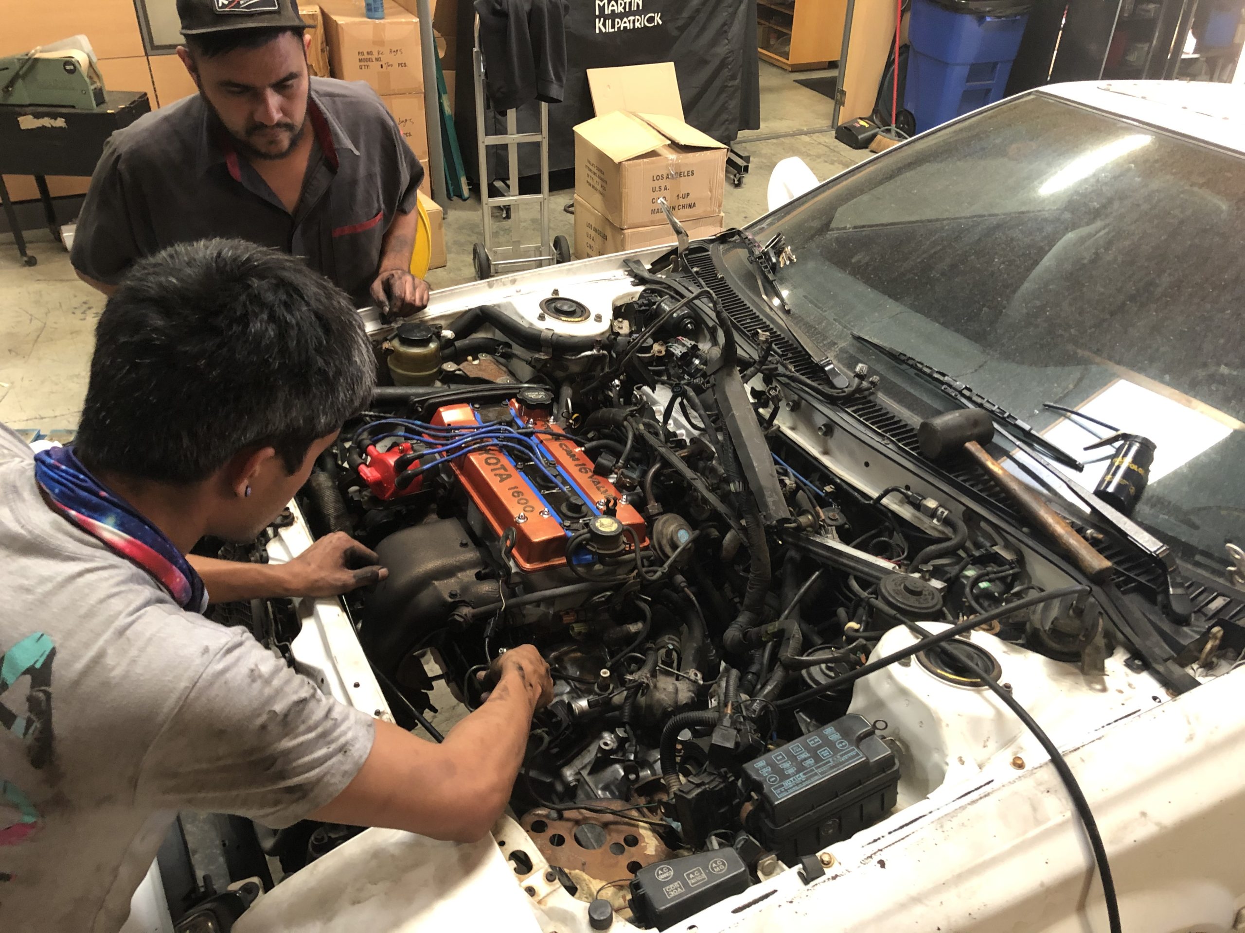 Two men lean in to look under the hood of the AWDROLA, inspecting the engine.