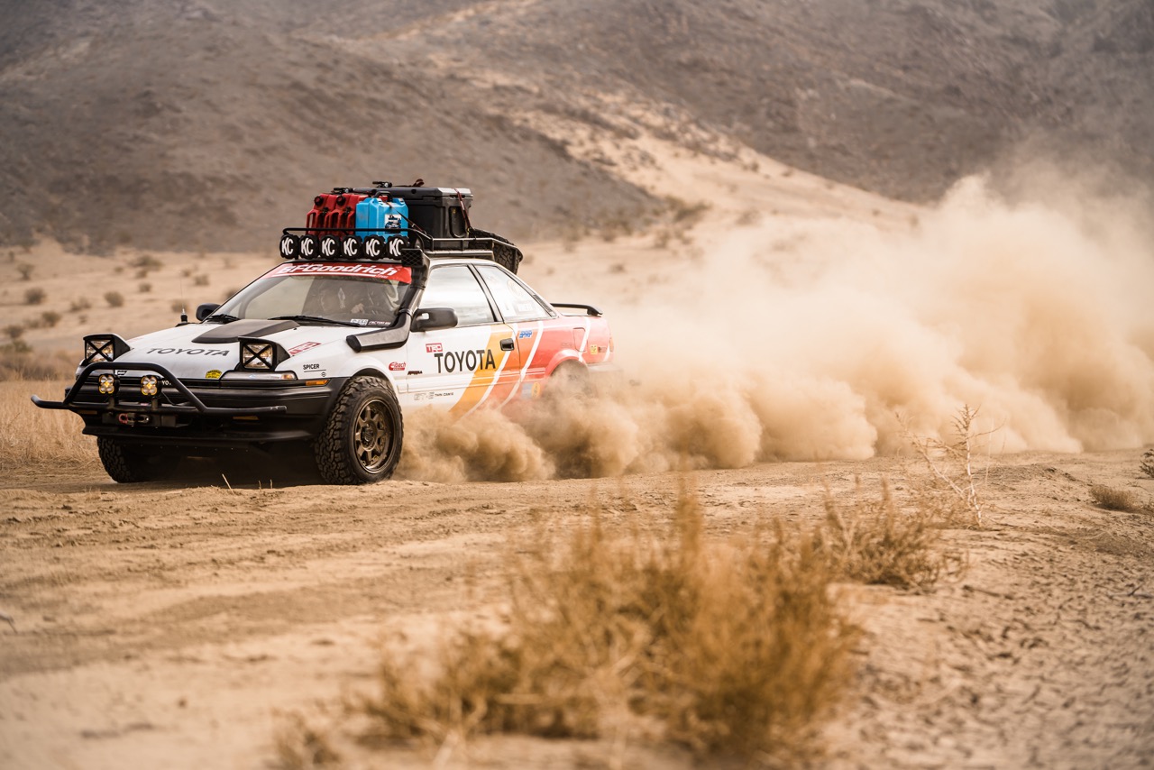An off-road Toyota Corolla speeds on a dirt road.