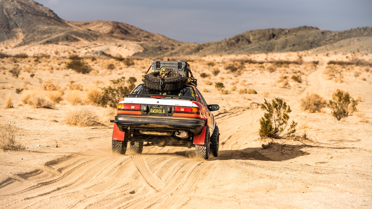 A rear view of a 4x4 Toyota Corolla driving on a dirt road.