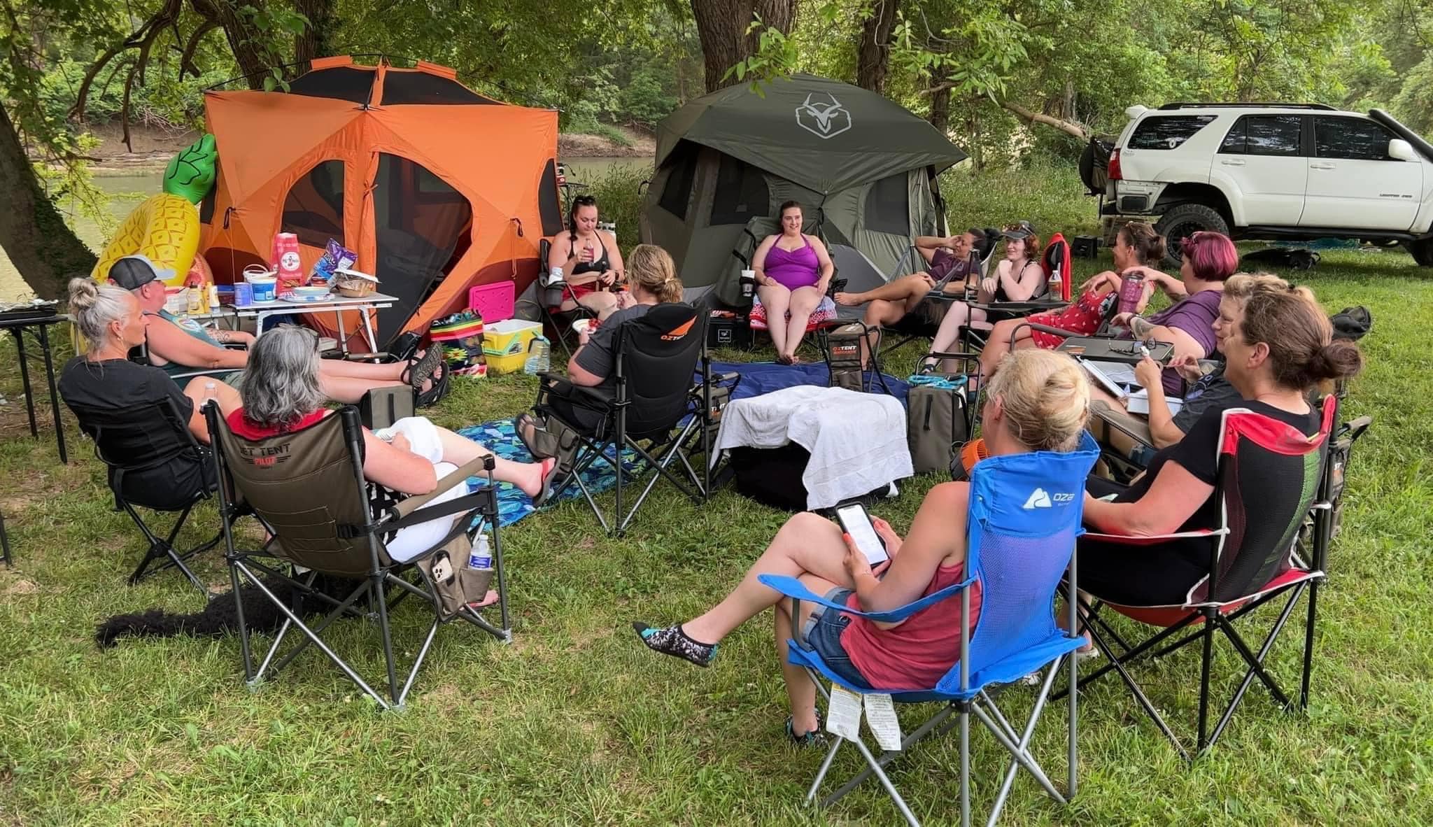 Attendees of a Lady Ovlerander Radio camping weekend sit in camp chairs in a circle chatting and eating lunch.