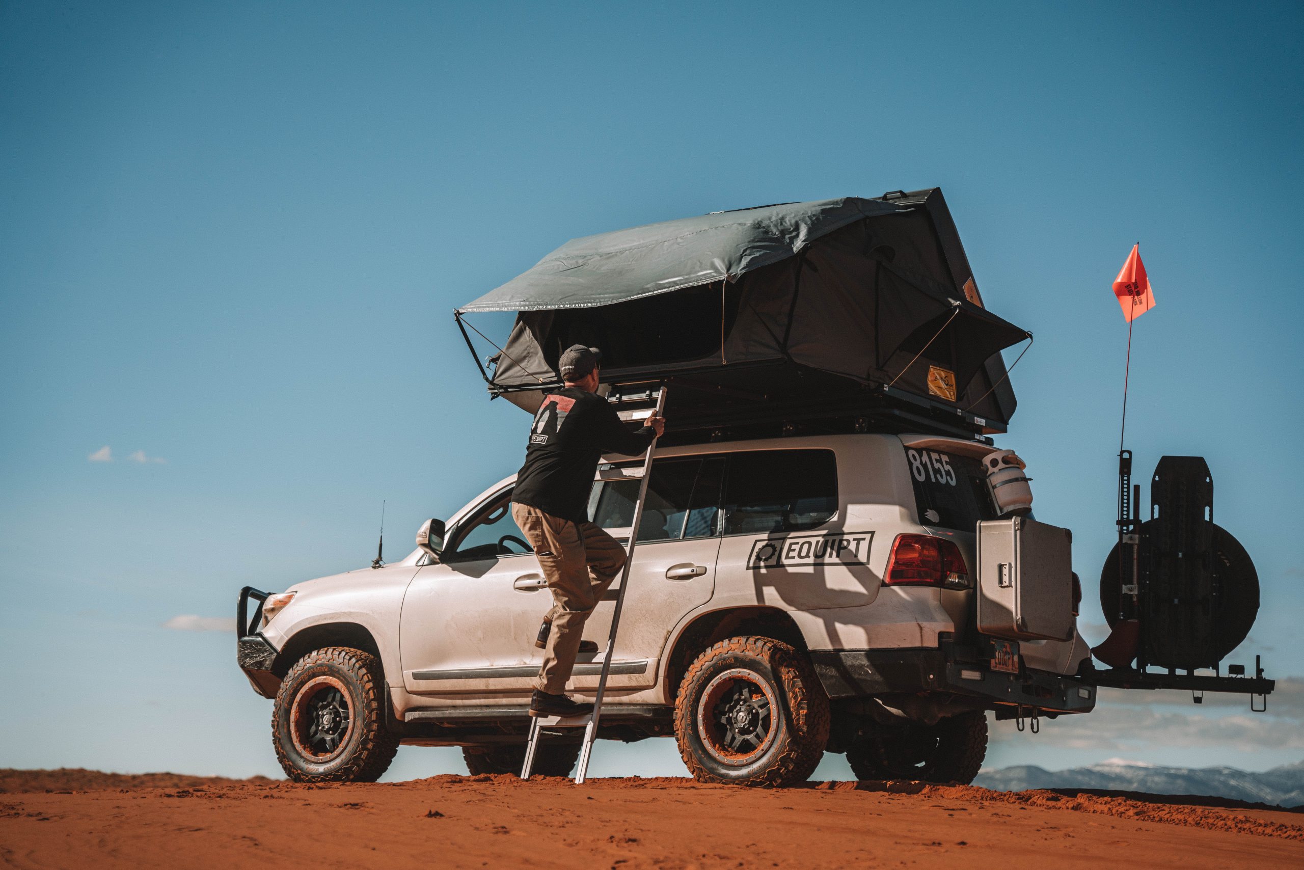 A man clmibs up the ladder to the Eezi-Awn roof top tent atop an SUV. 