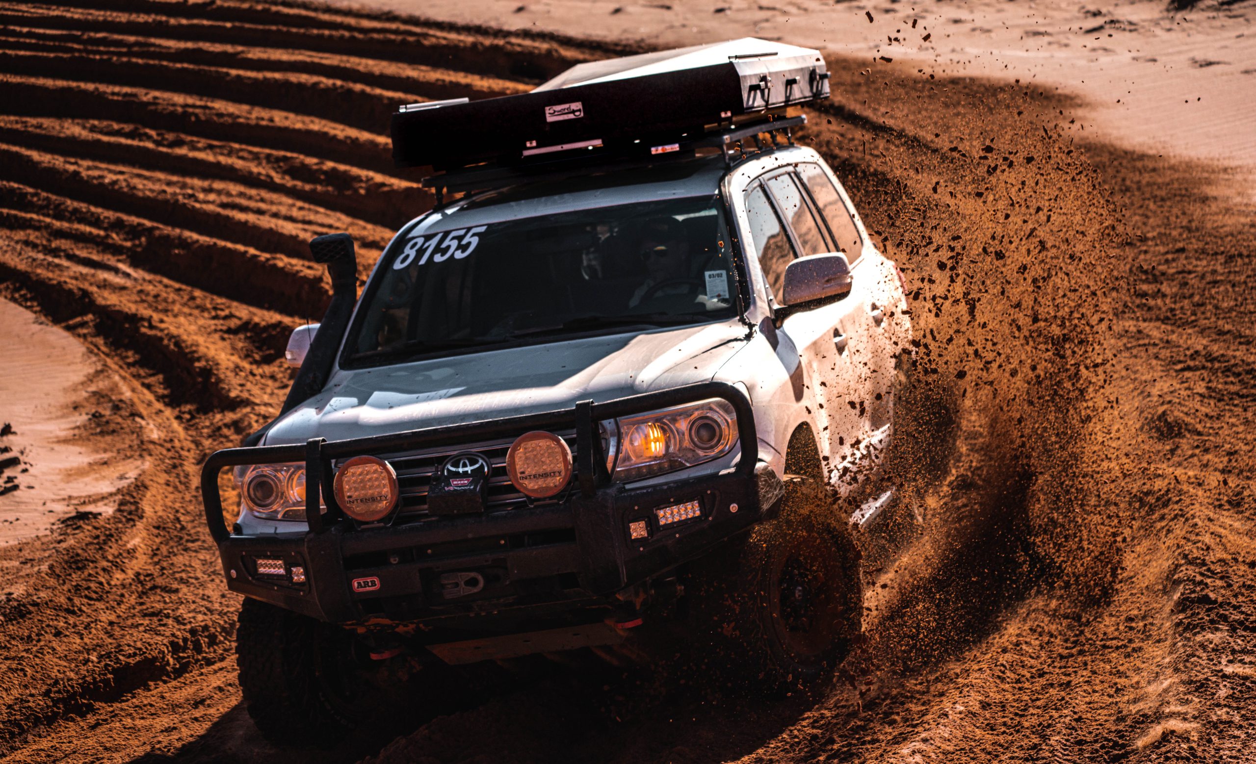 An SUV rips through mud, kicking up dirt, with the Eezi-Awn roof top tent secured on the roof.