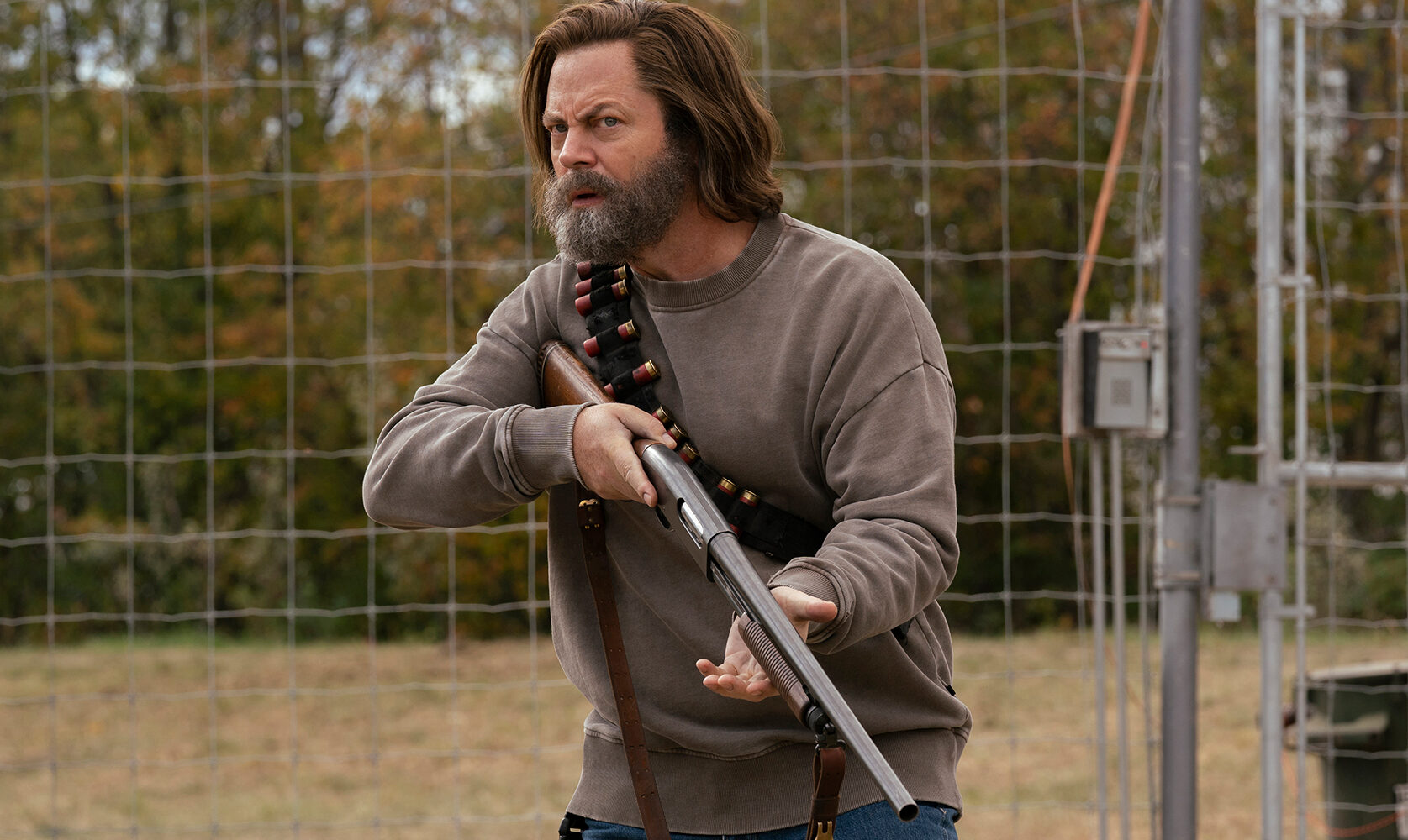A screenshot from The Last of Us shows Nick Offerman, a beareded man with long hair, holding a shotgun.
