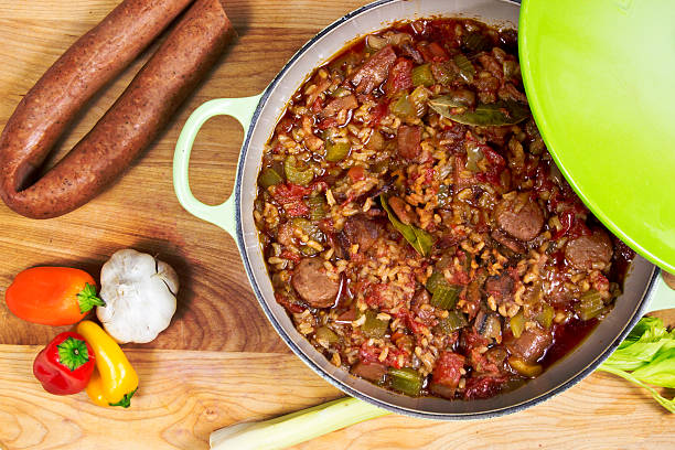 Dutch oven full of jambalaya on cutting board with andouille sausage, garlic, bell peppers and celery.