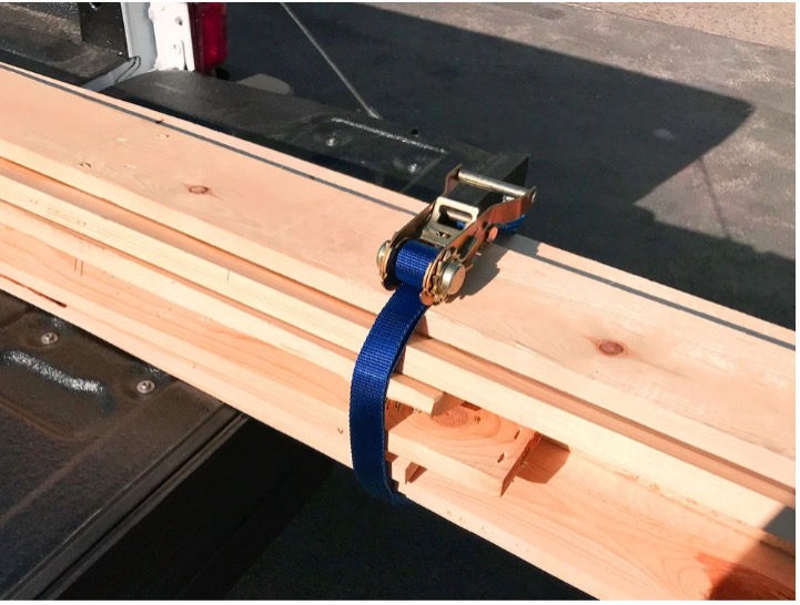 Mac's Tie Down blue ratchet strap secures a bundle of wood in bed of truck.