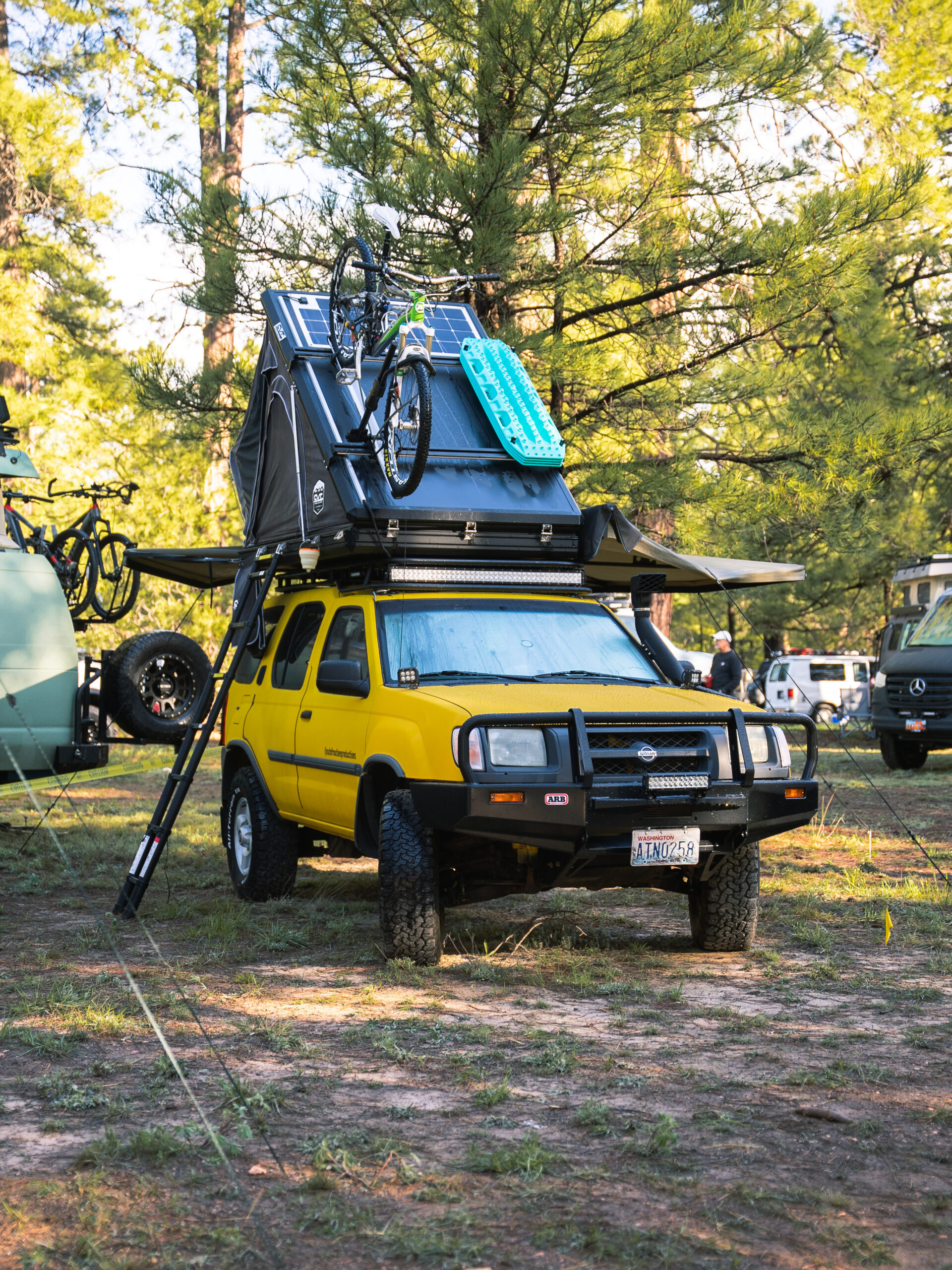 Yellow Nissan with a roof top tent deployed with a bike attached to the top.