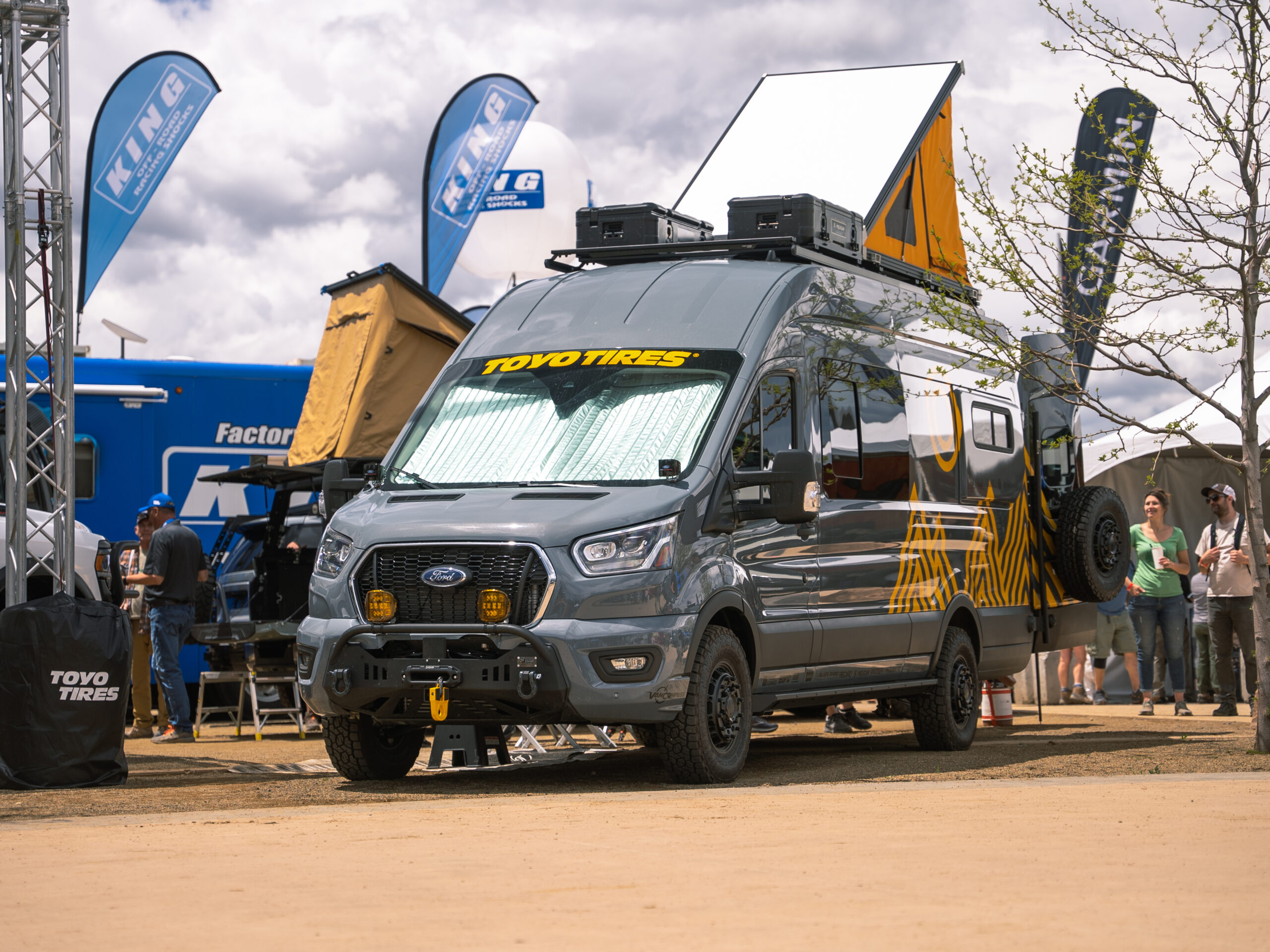 A gray Ford van with yellow graphics and yellow pop-up roof top tent.