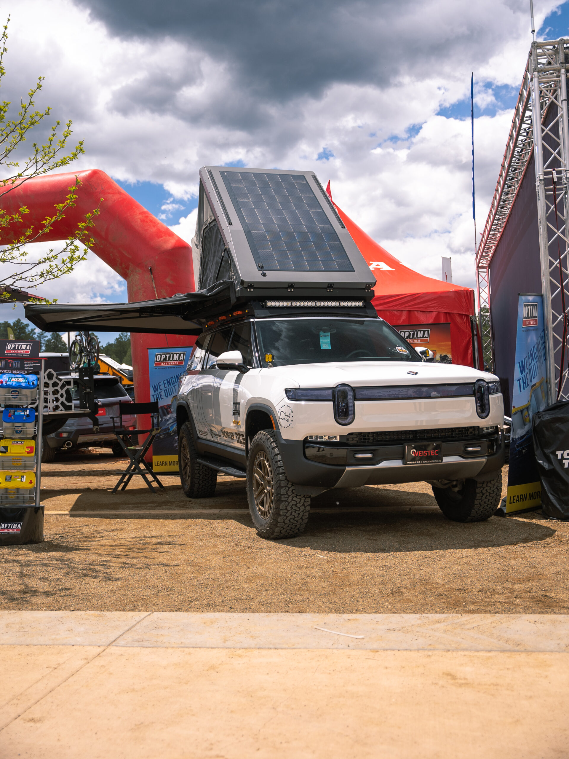 A white Rivian with awning and pop-up roof top tent at Overland Expo West.