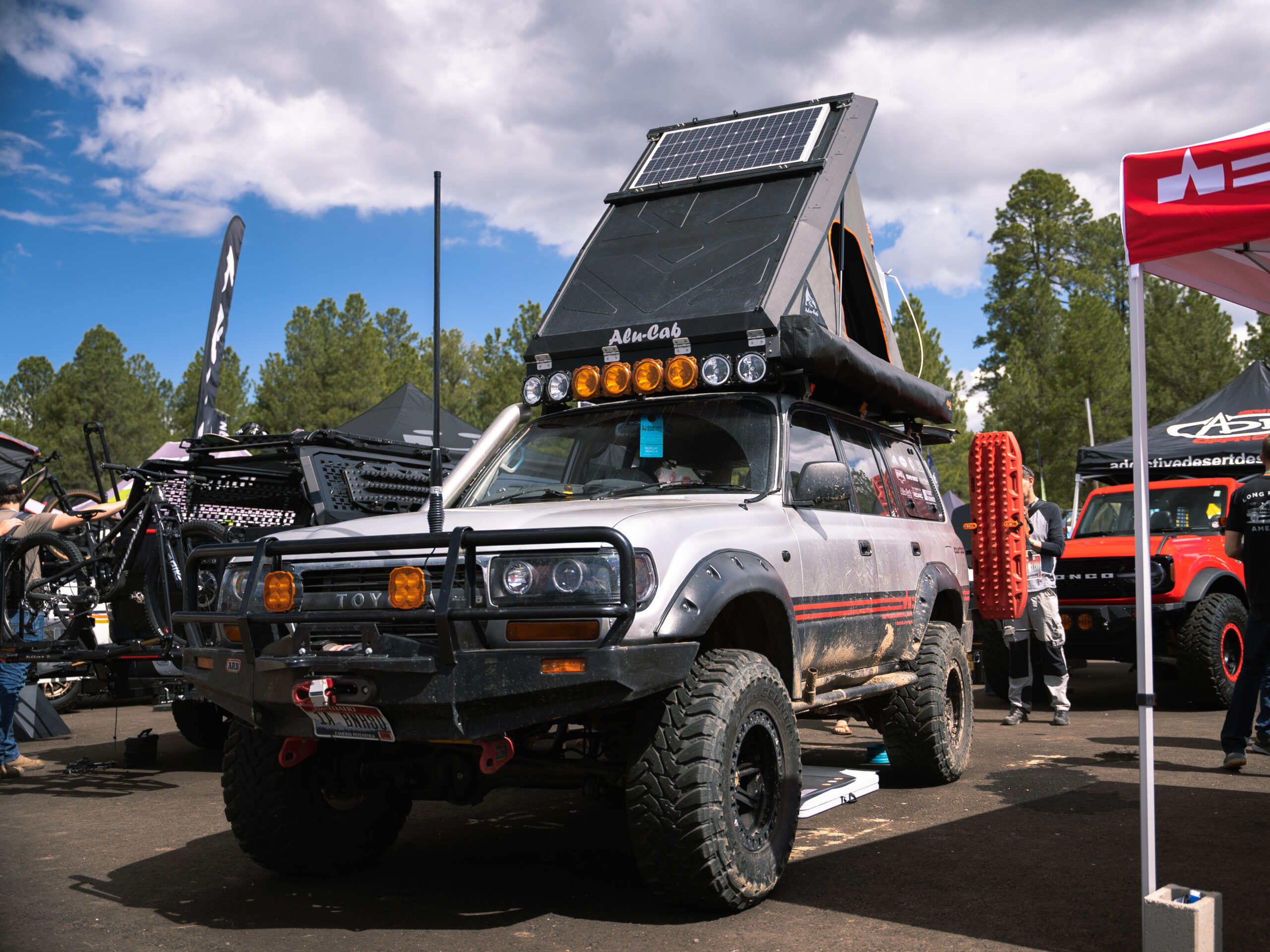 A gray 4Runner with orange details and light bars with Alu-Cab pop top tent.