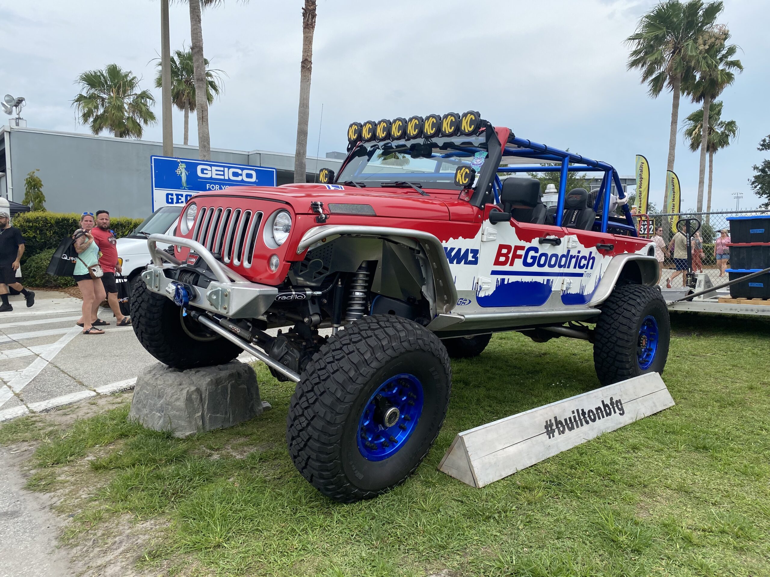 Red, white, and blue Jeep with BFGoodrich emblem on driver door parked on grass.